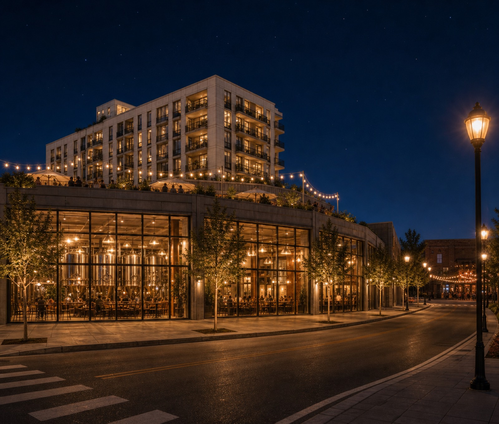 Night view from North St: the double-height brewery hall glowing with its tanks visible, the string-lit event terrace above, and lit residential balconies behind